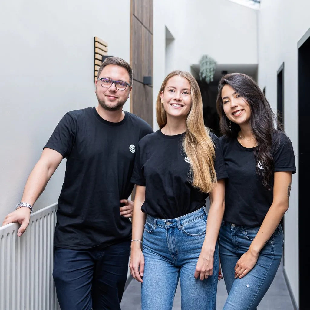 Three people in black t-shirts and jeans stand together in a hallway with Nordic acoustic panels on the wall, smiling at the camera.